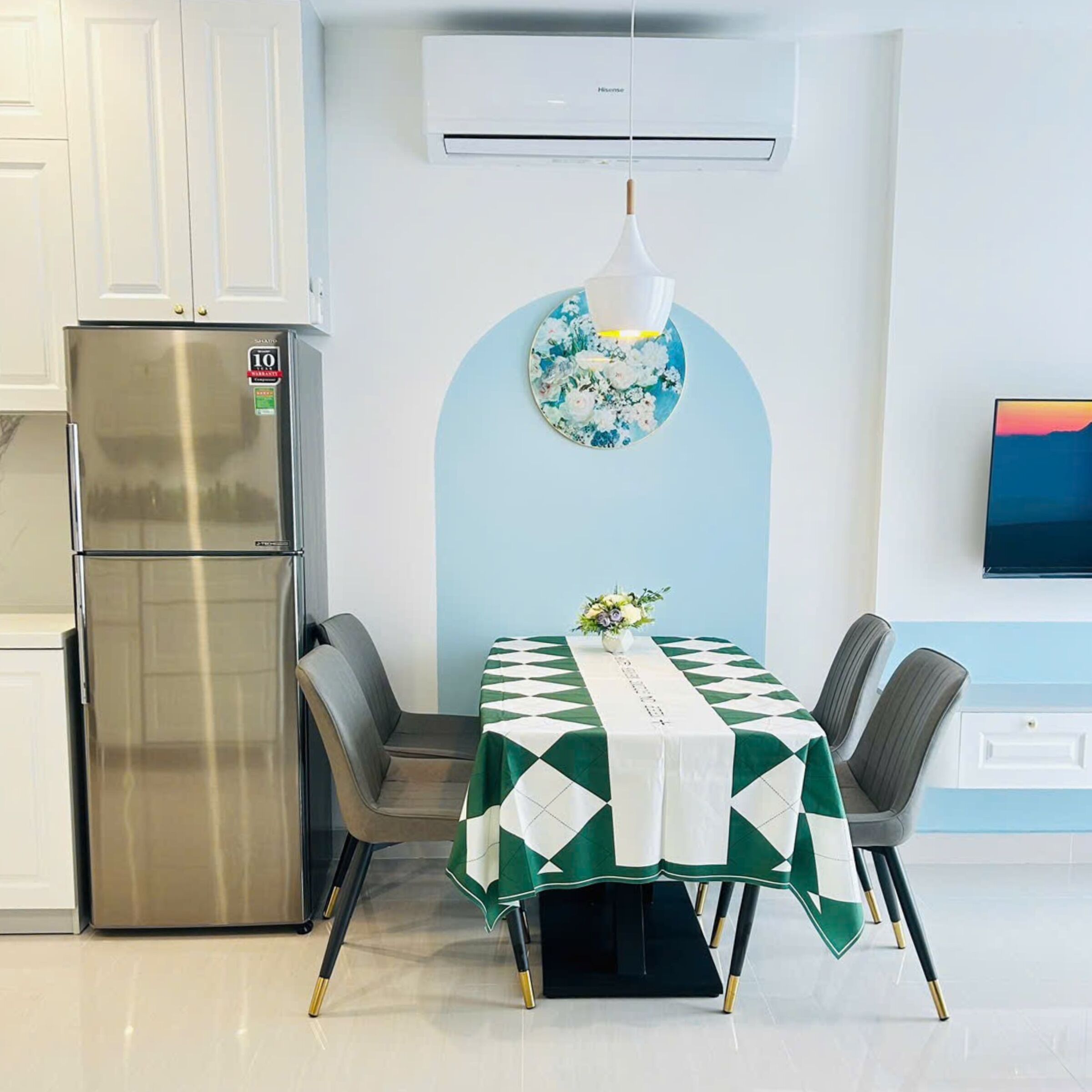 A modern kitchen with a stainless steel refrigerator, a dining table with a green and white checkered tablecloth, and a wall-mounted air conditioner.