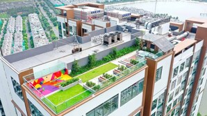 Un edificio alto con jardín en la azotea, varios balcones y vistas a un paisaje urbano y una masa de agua.