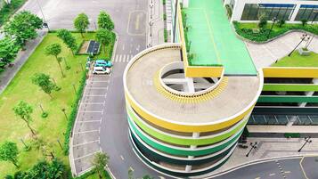 Una estructura de estacionamiento de varios niveles con diseño circular, rodeada de áreas verdes y una carretera con vehículos.