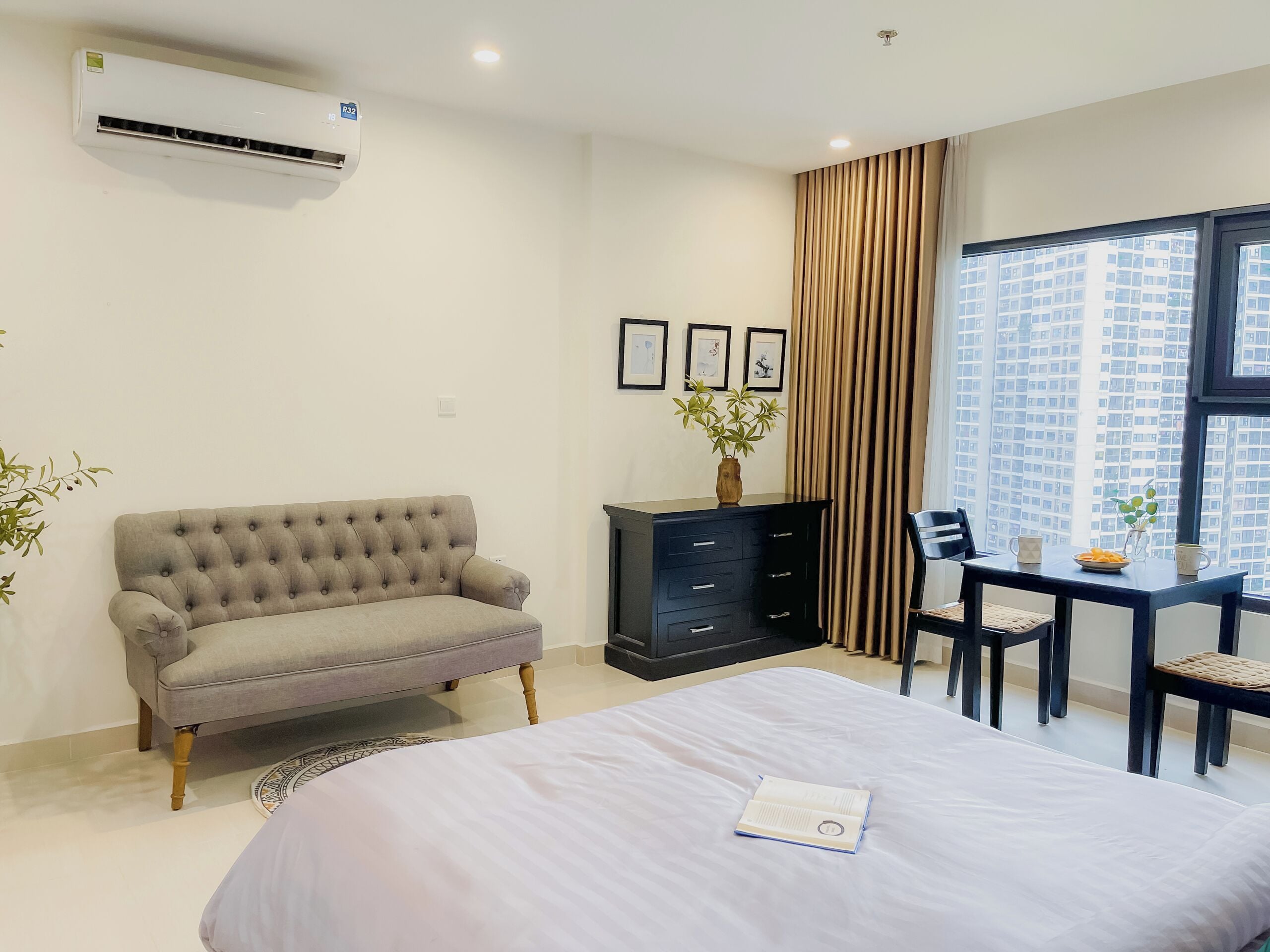 Quarto com cama, sofá, escrivaninha com cadeiras, cômoda e janela com vista para a cidade.