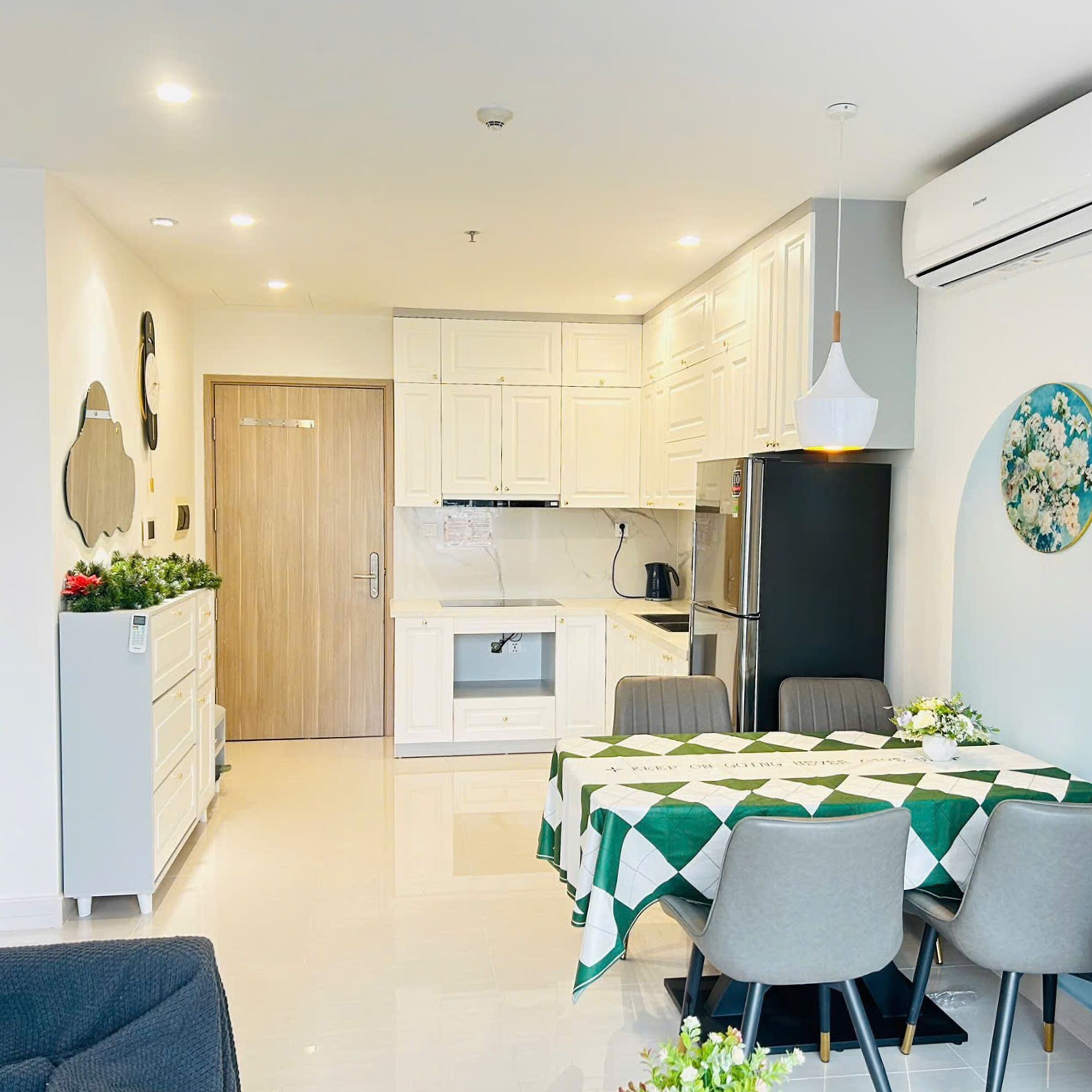 Una cocina moderna con armarios blancos, un refrigerador negro y una zona de comedor con mantel a cuadros verde y blanco.