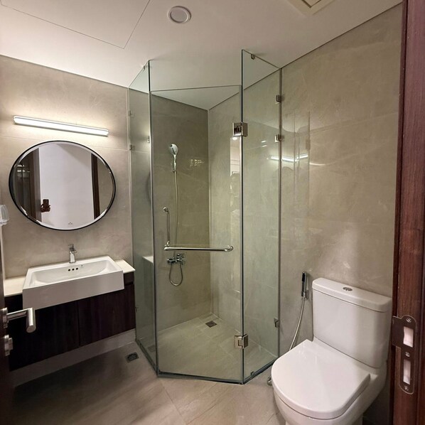 Un ba ño moderno con ducha envuelta en vidrio, un espejo redondo, lavamanos blanco y un inodoro.