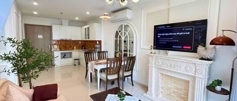 A modern living room with a sofa, a coffee table, a fireplace, a TV, and a dining area with chairs and a table.