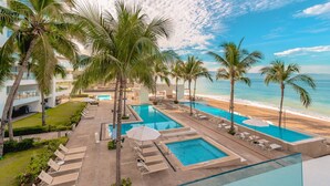 A resort with multiple swimming pools, palm trees, and a beach view.