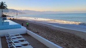 A beach with a pool area, including lounge chairs and a flag.
