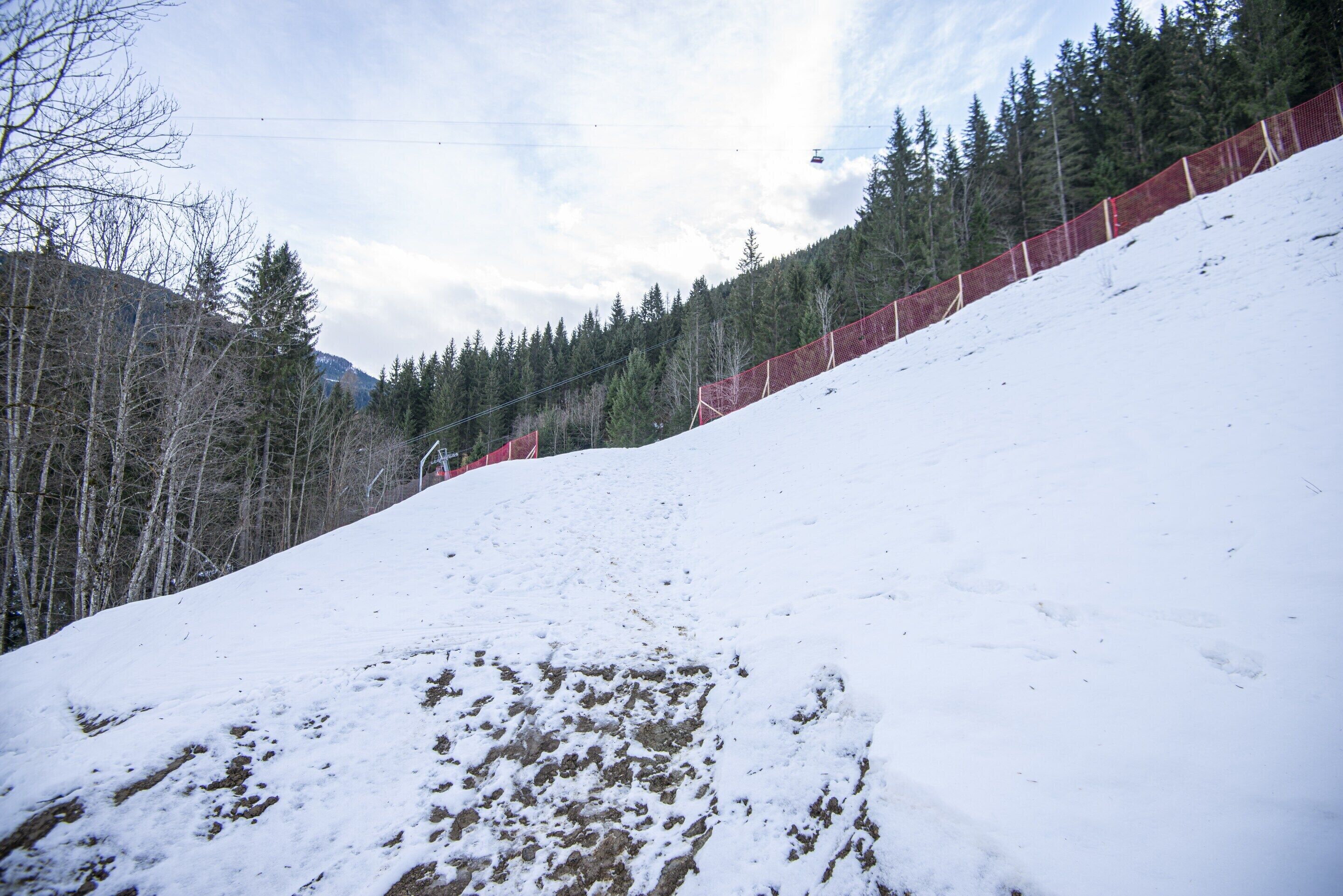 A snow-covered slope with a ski lift in the background and a forested mountain.