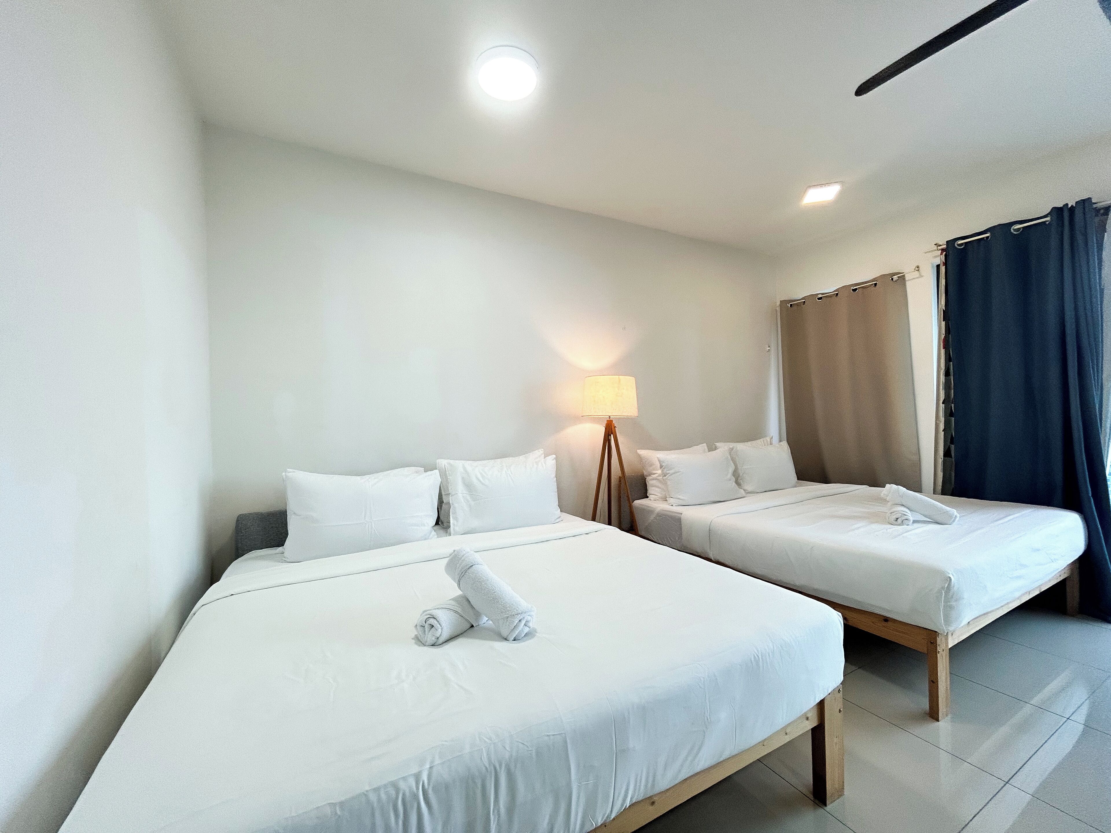 A hotel room with two single beds, a bedside table with a lamp, and a window with curtains.