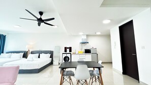 Habitación de hotel moderna con cama, escritorio, silla, ventilador de techo, lavadora, microondas y una pequeña cocina.