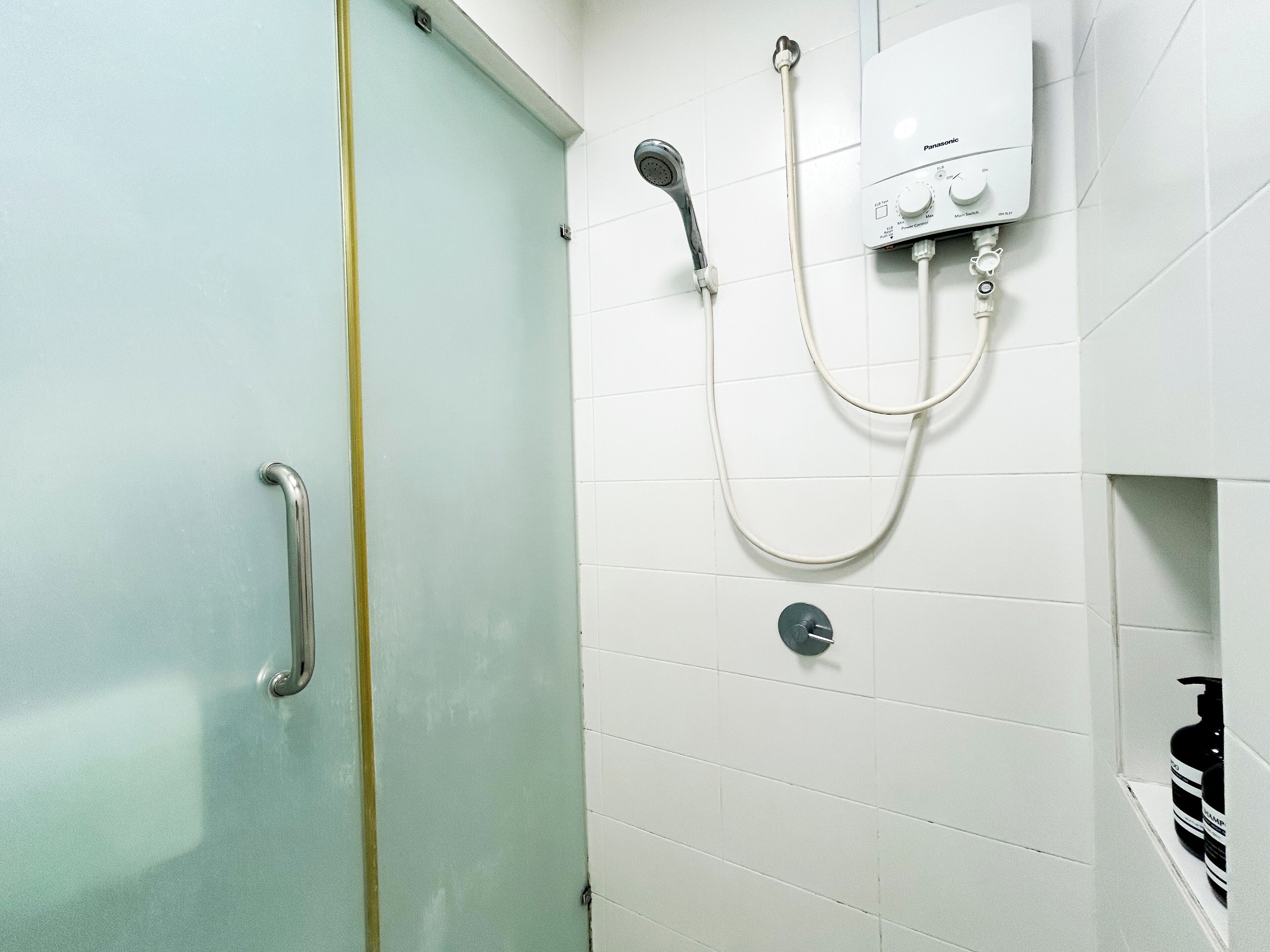 A bathroom with a glass door, a shower with a handheld showerhead, and a control panel.