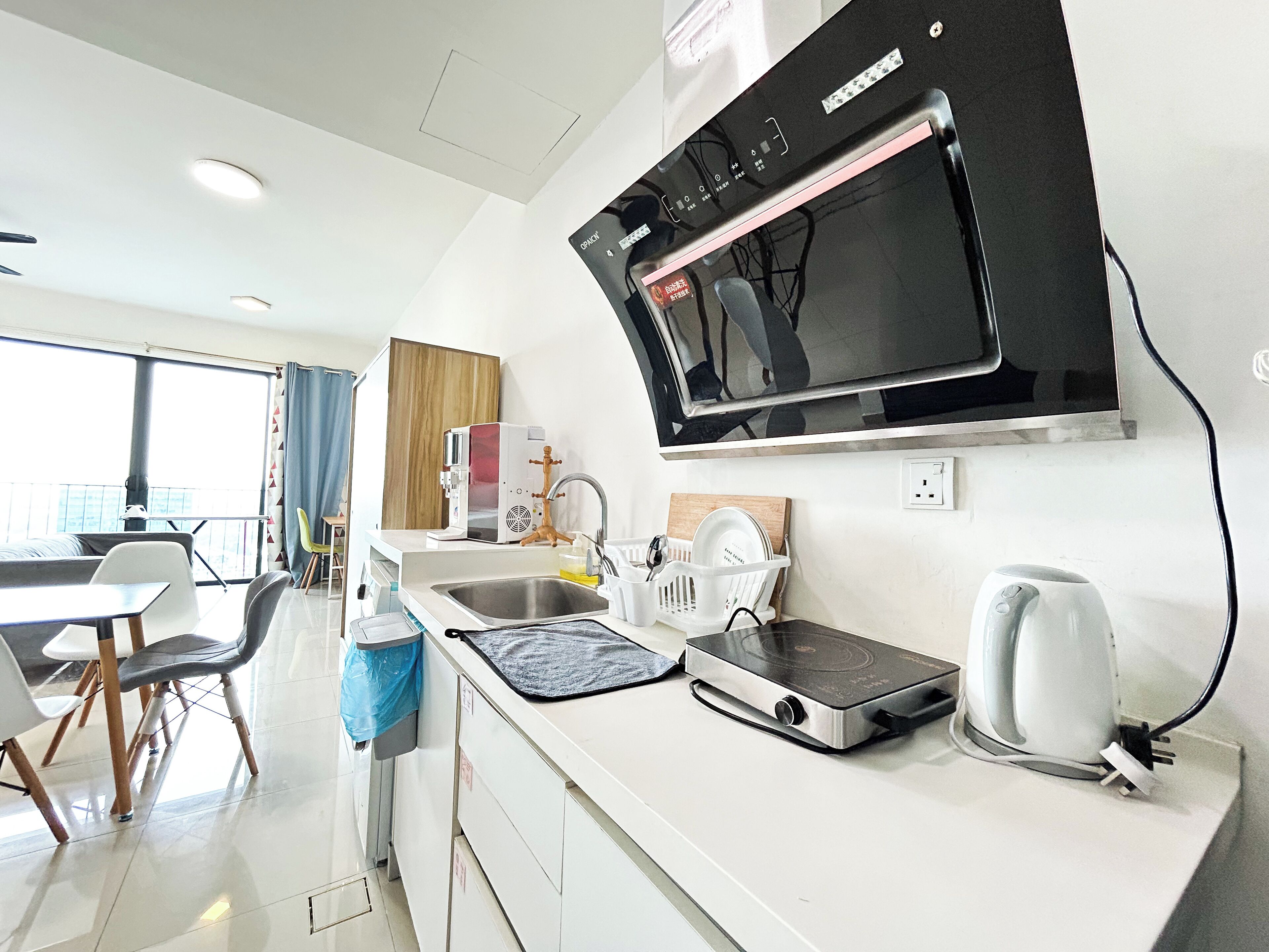 Une cuisine moderne équipée d’un four à micro-ondes, d’une bouilloire et d’une cuisinière électrique. On y trouve un évier avec un égouttoir et une fenêtre donnant sur un balcon.