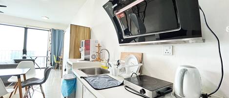 Une cuisine moderne équipée d’un four à micro-ondes, d’une bouilloire et d’une cuisinière électrique. On y trouve un évier avec un égouttoir et une fenêtre donnant sur un balcon.