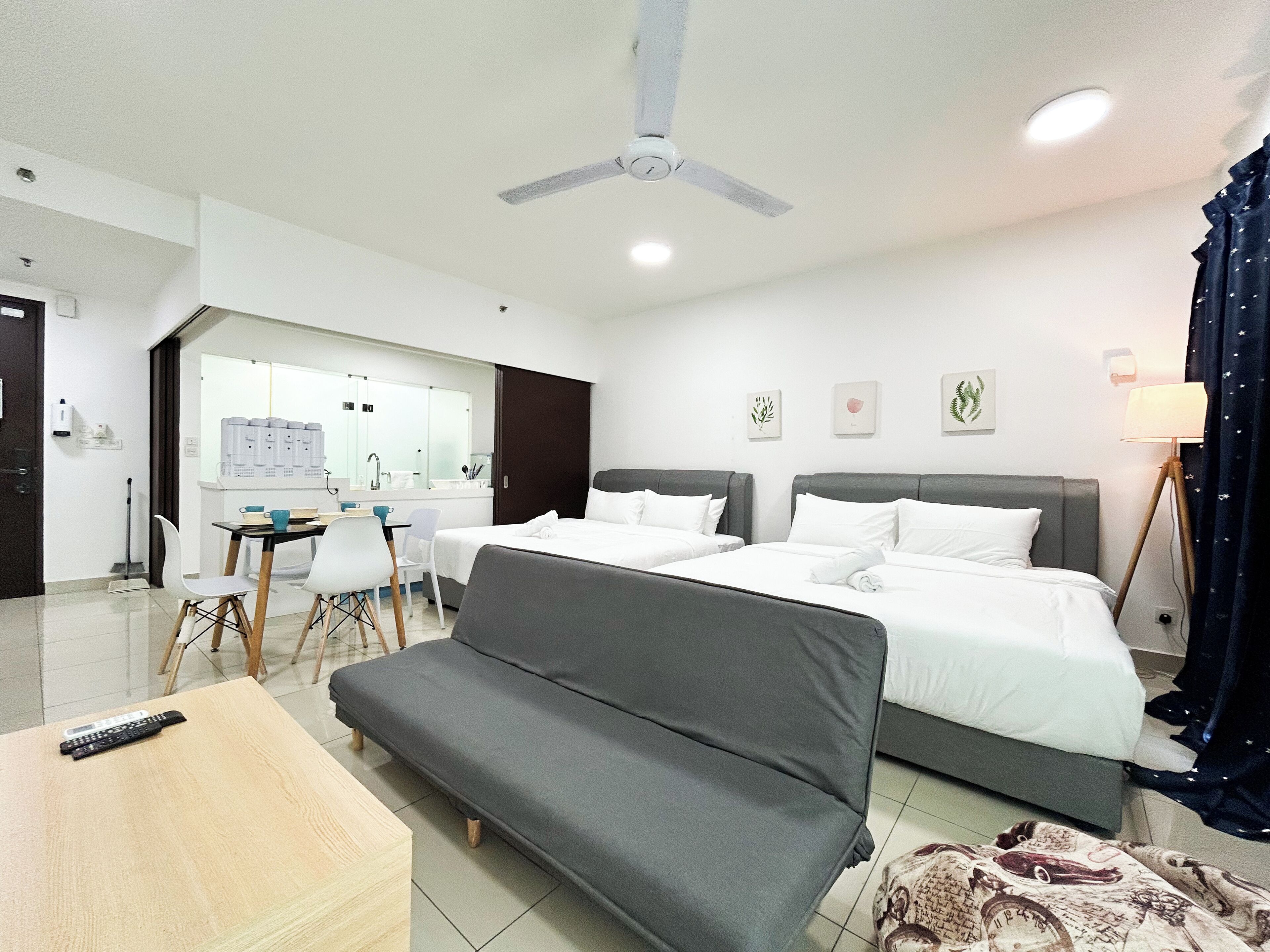 A hotel room with two beds, a sofa, a desk with chairs, a ceiling fan, and a lamp.