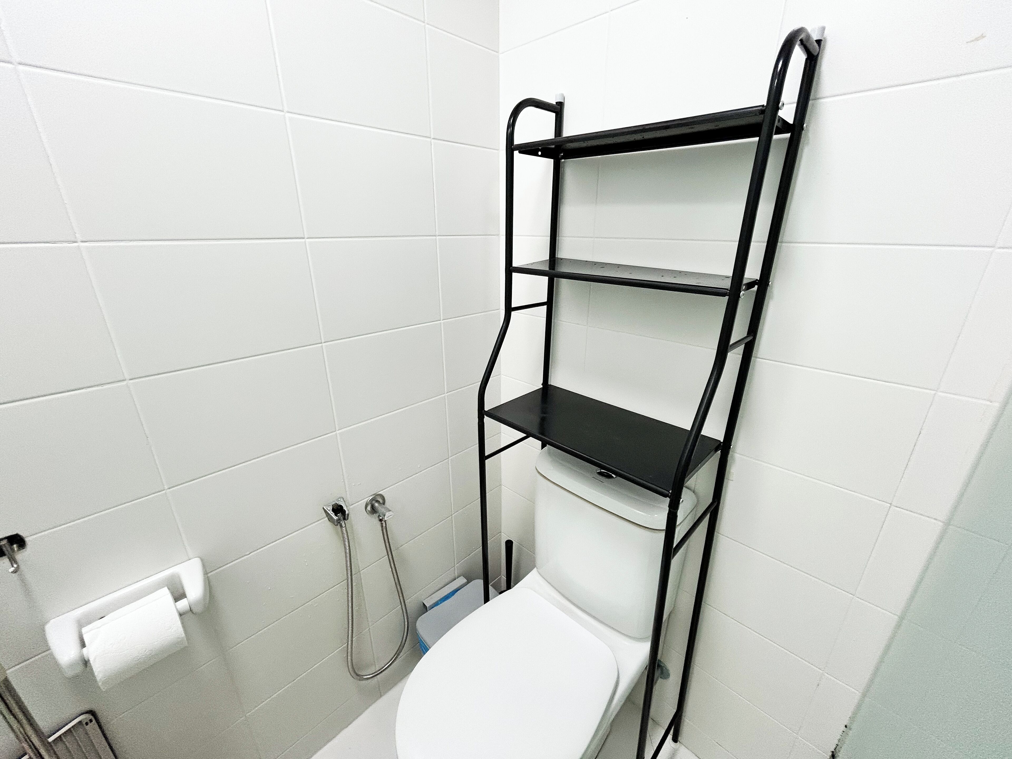 A bathroom with white tiles, a toilet, a black metal shelf unit, and a towel rack.