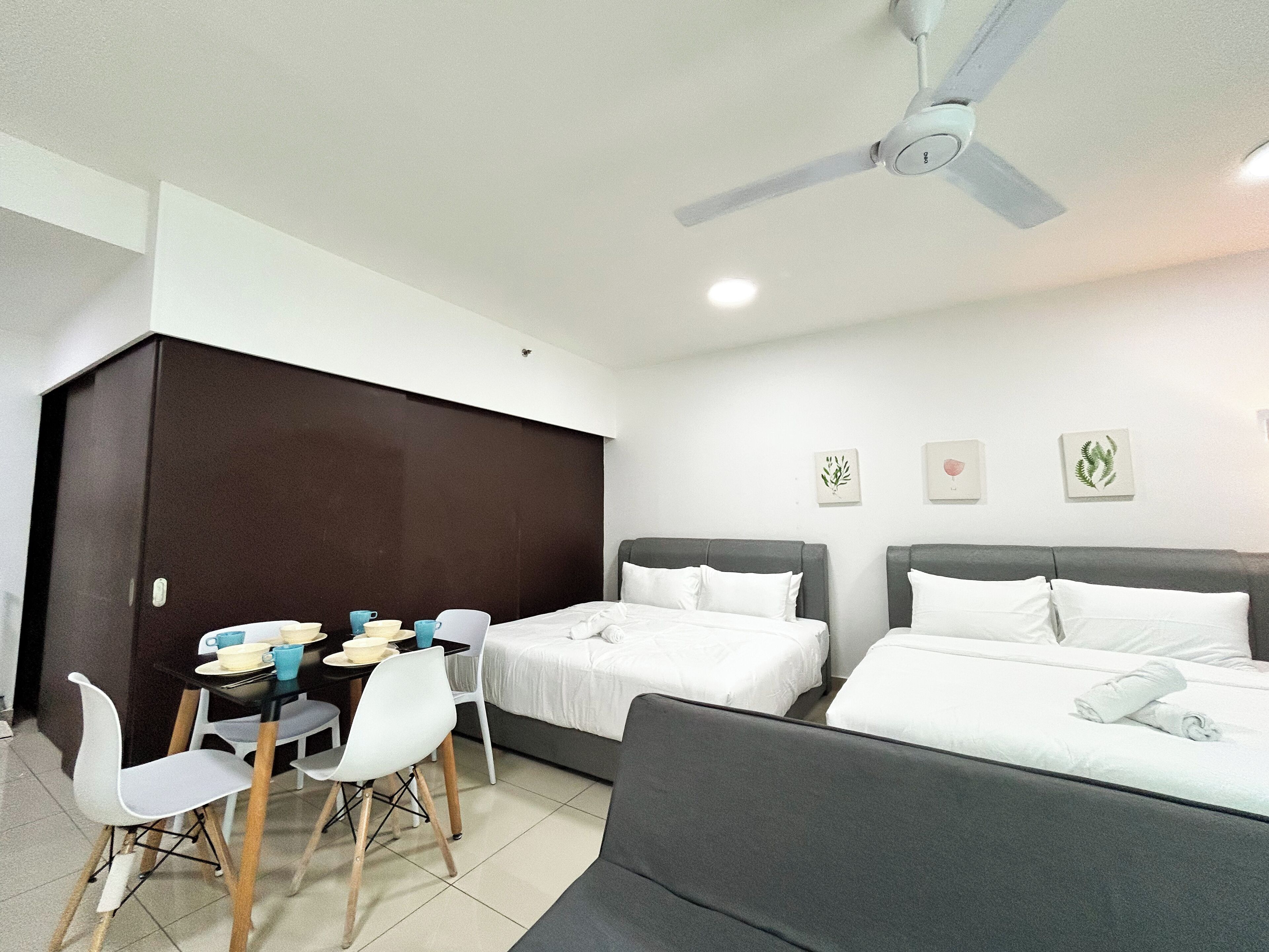 A hotel room with two beds, a dining table with chairs, a ceiling fan, and wall art.