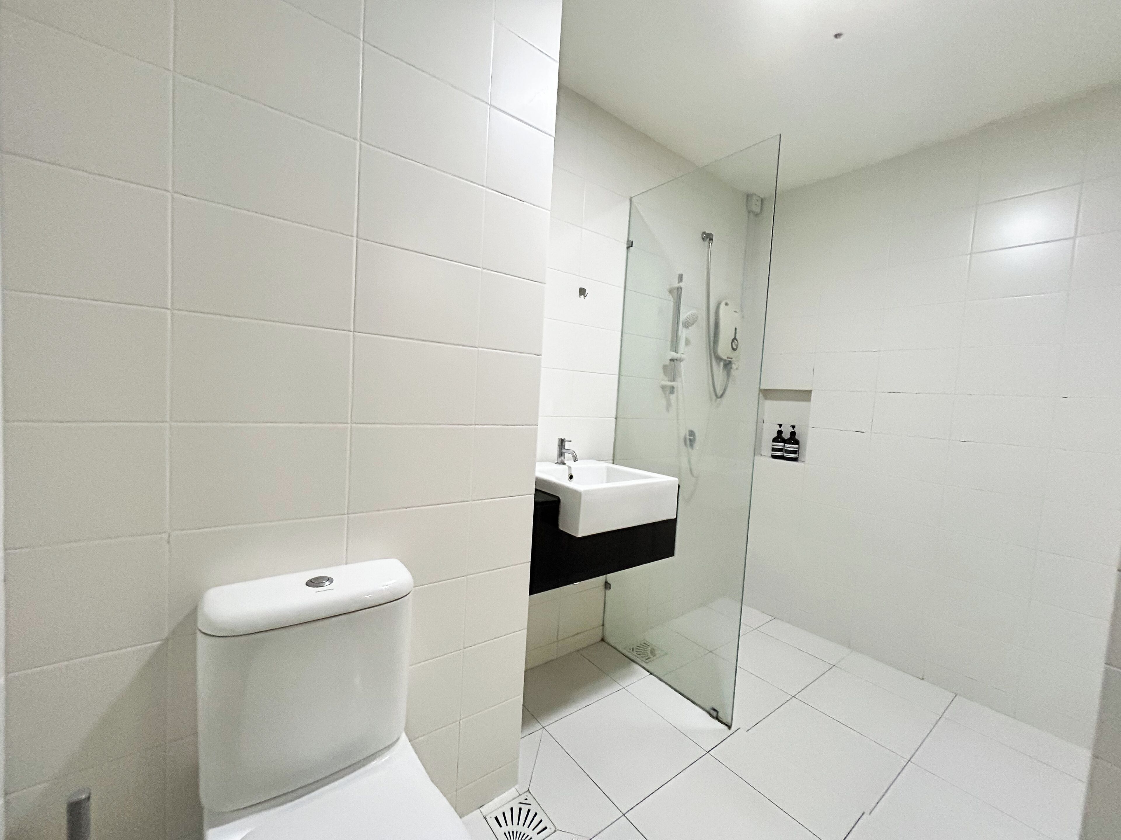 Un baño moderno con azulejos blancos, inodoro, lavamanos y cabina de ducha con mampara de vidrio.