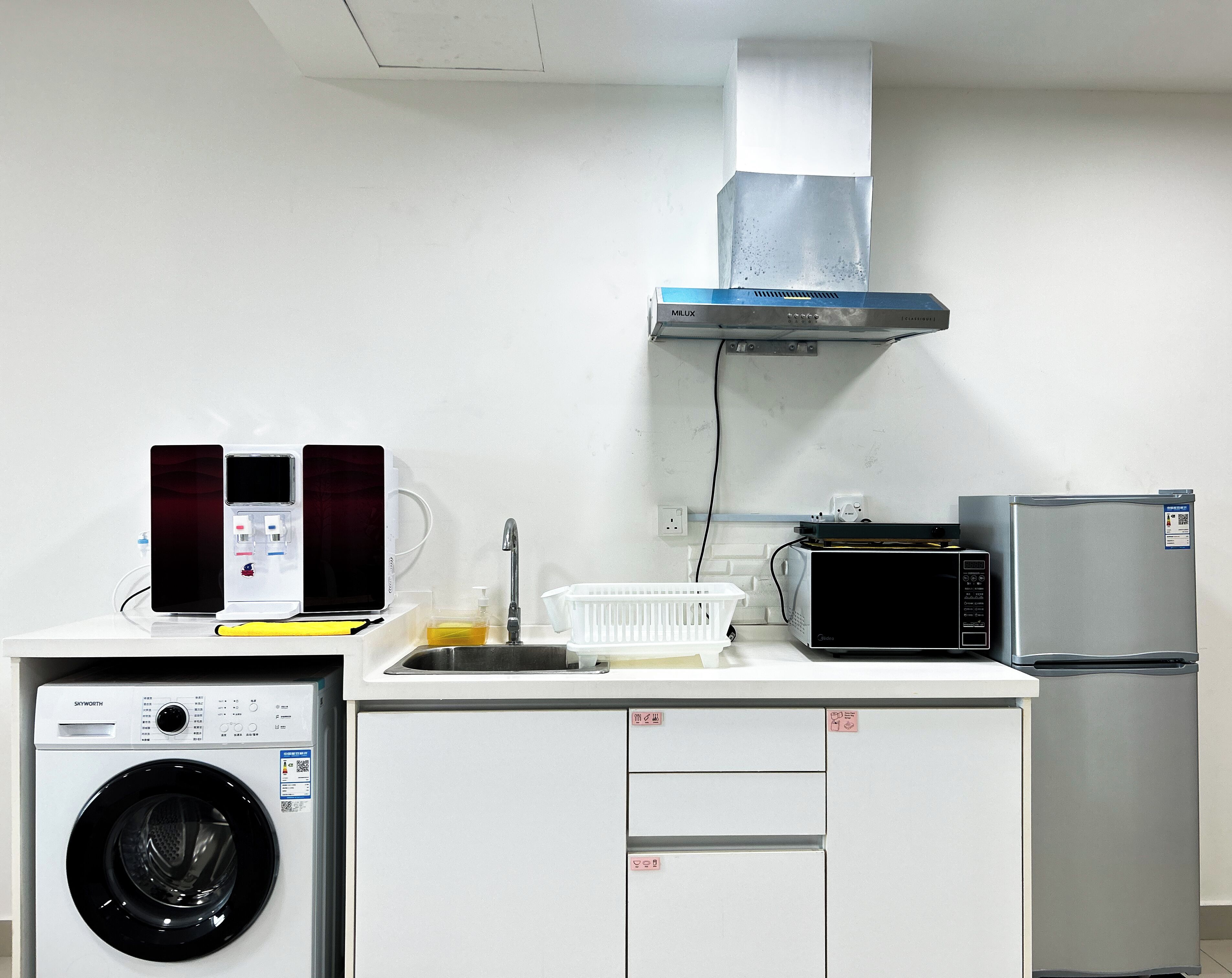 A compact kitchen with a washing machine, microwave, refrigerator, and a small sink.