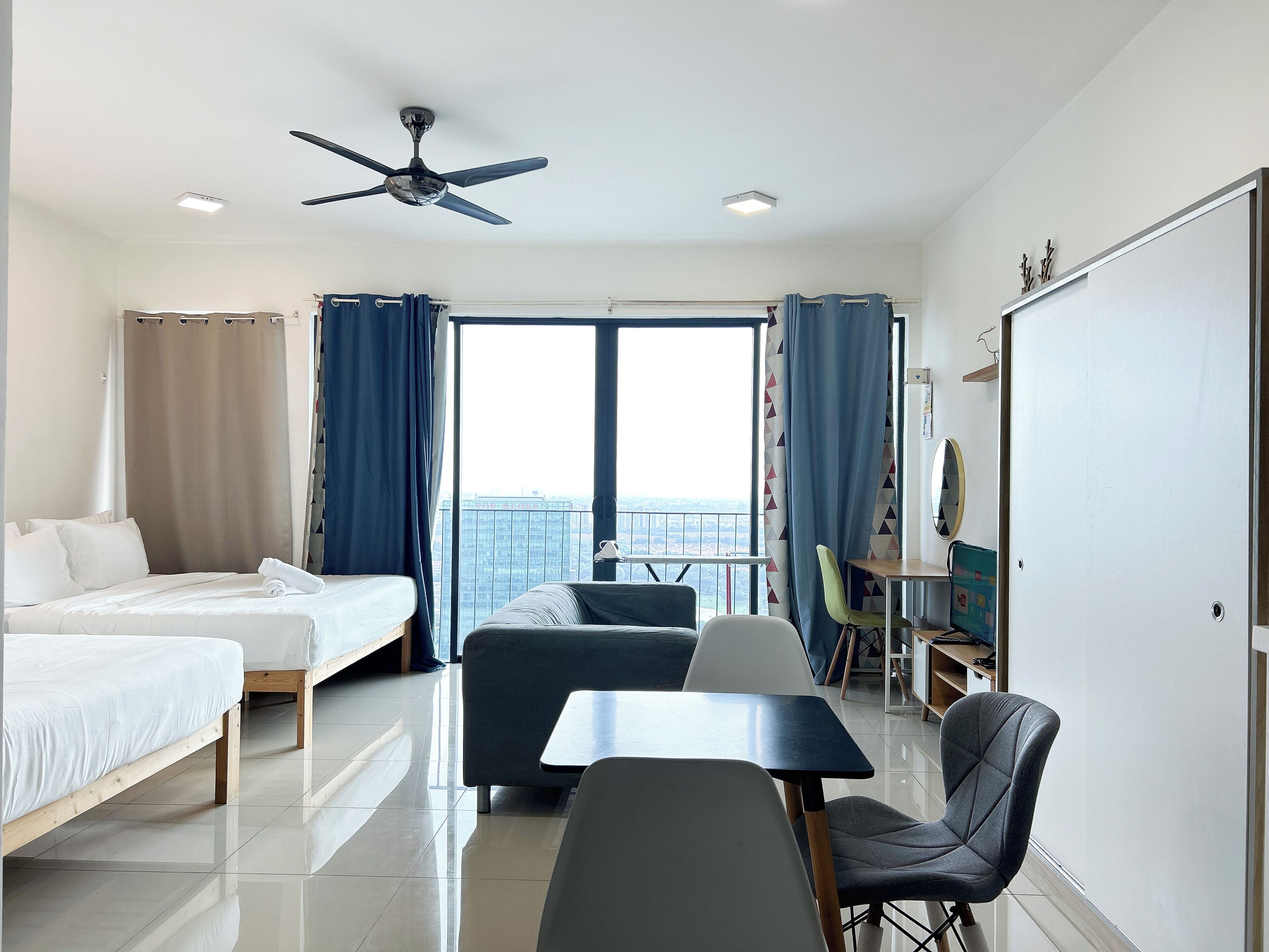 A hotel room with a bed, a desk, a chair, a ceiling fan, and a large window with curtains.