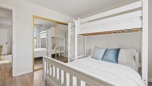 Una habitación con literas, un armario blanco y un espejo con marco dorado.