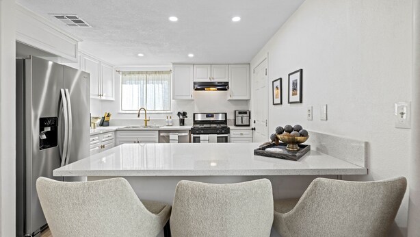Una cocina moderna con armarios blancos, un refrigerador de acero inoxidable, una isla central con sillas y una estufa.