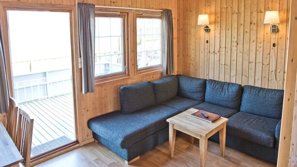 A cozy cabin interior with a wooden ceiling, a gray sofa, a small wooden table, and two windows with curtains. - 4 Person Holiday Park Home in Kinsarvik (Ullensvang)