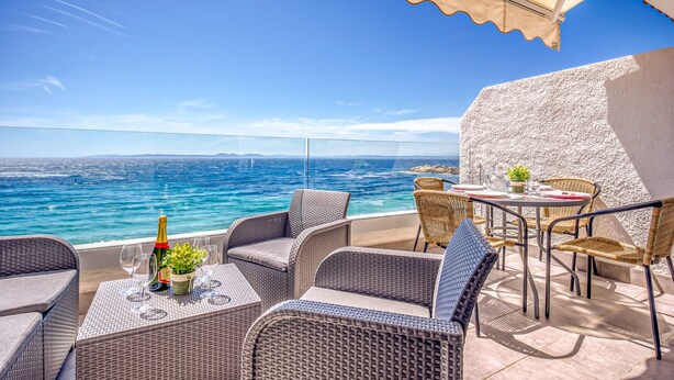 A terrace with wicker furniture, a table with a bottle of champagne, and a view of the sea. - Beachfront Apartment in Platja Almadrava (Roses)