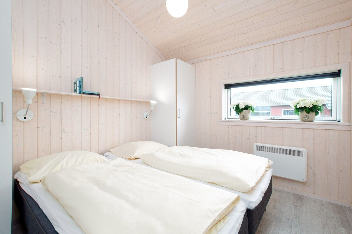 A bedroom with two beds, a window with plants, a white wardrobe, and a ceiling light.