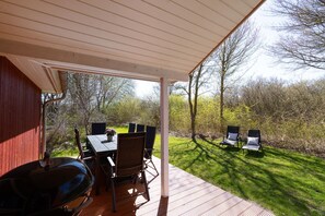 A covered patio with a table and chairs, a barbecue grill, and a view of a grassy area with trees.