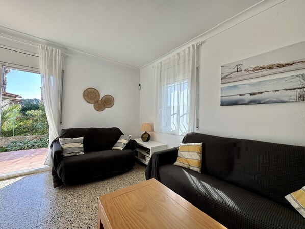 A living room with two black sofas, a wooden coffee table, a small white side table with a lamp, and a painting on the wall.
