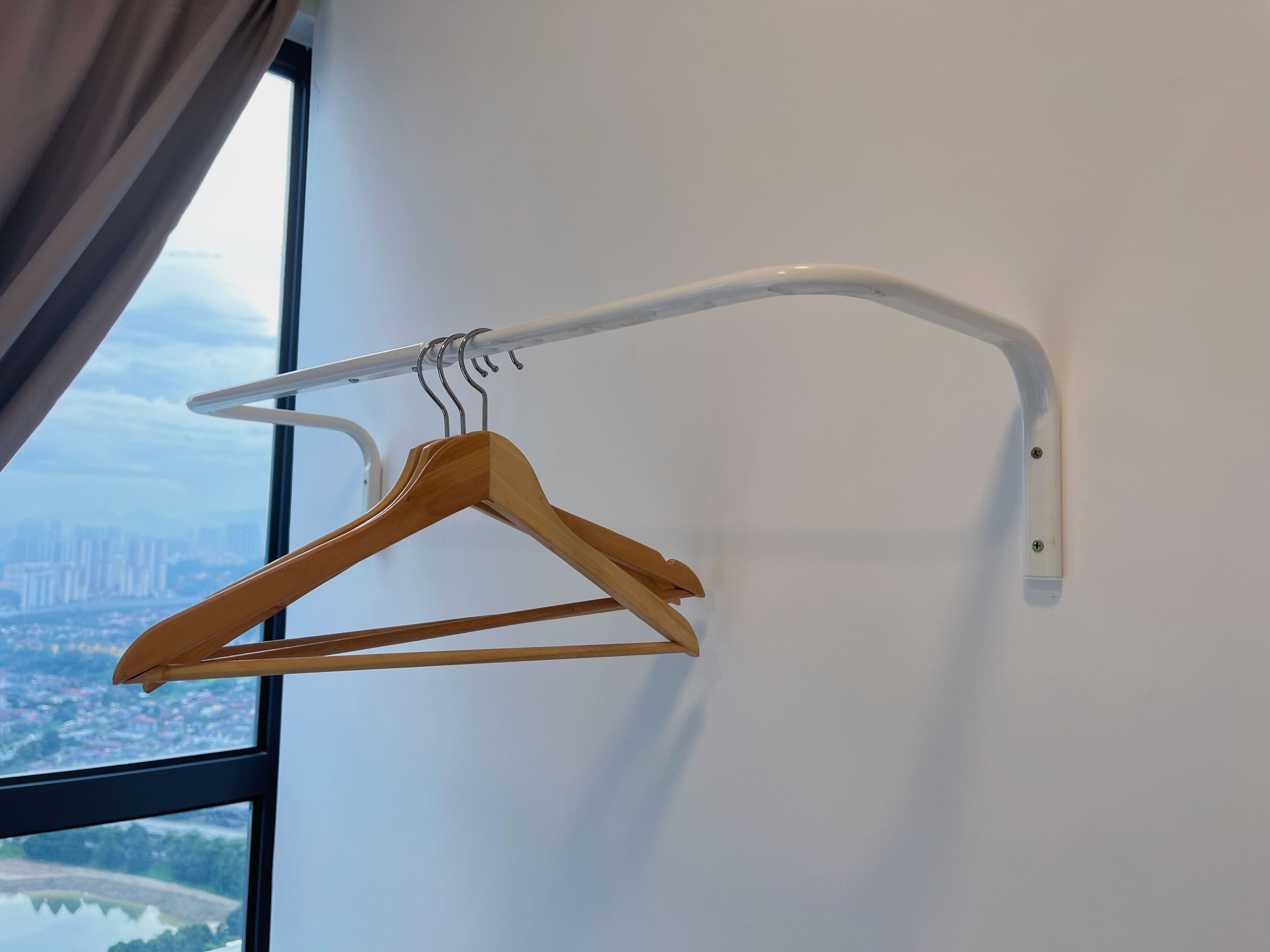 A wooden hanger on a white metal rack against a wall with a window.