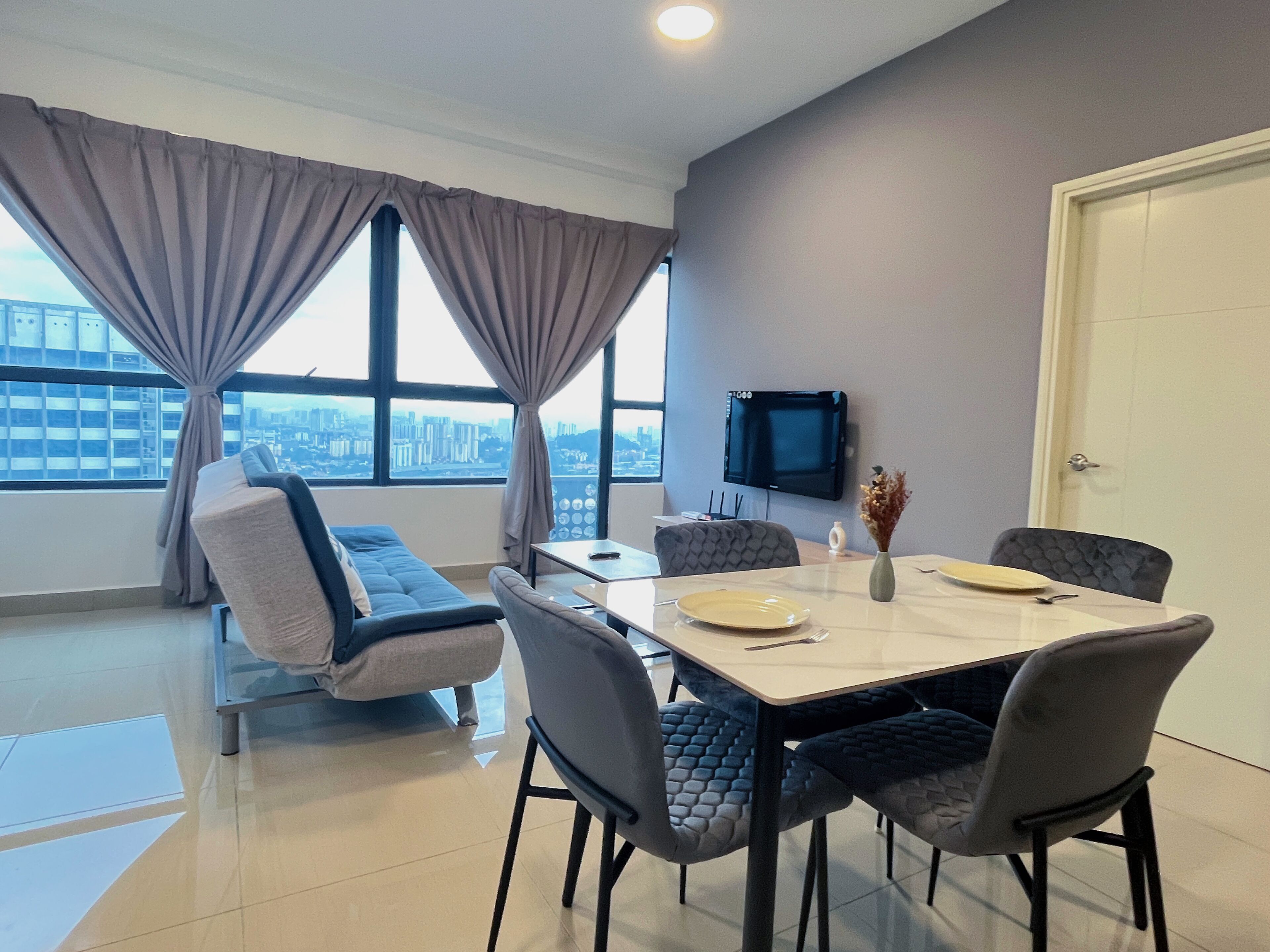 Un moderno comedor con una mesa preparada para cuatro personas, un sofá y un televisor montado en la pared.