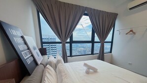 Een hotelkamer met een bed, uitzicht op de stad door grote ramen en een wandairconditioner.