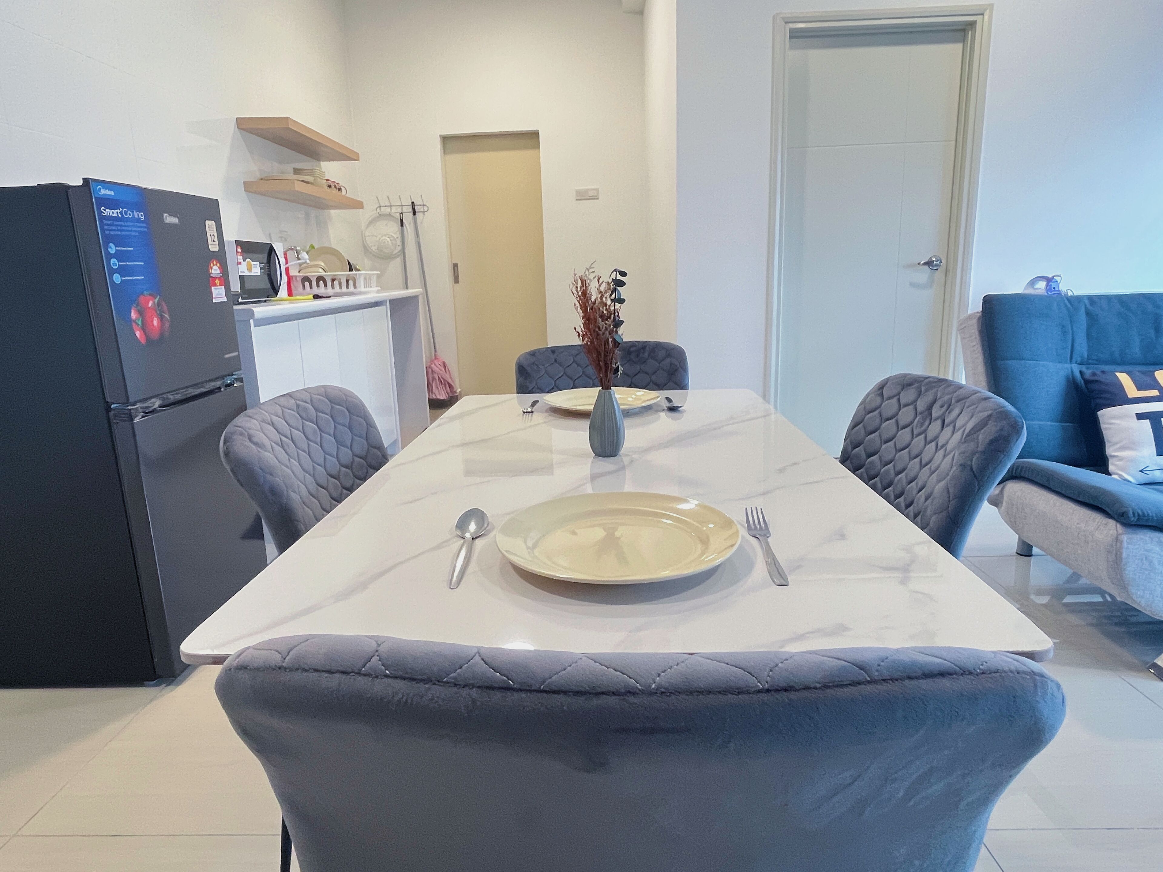 Une cuisine moderne équipée d’un réfrigérateur, d’une table à manger pour deux personnes et d’un canapé bleu dans l’espace salon.