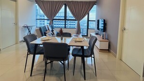 Een moderne eetruimte met een tafel voor vier personen, twee ramen met gordijnen, een flatscreen televisie op een standaard en uitzicht over de stad.