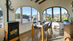 Ein Zimmer mit Kamin, großen Bogenfenstern, einem Esstisch mit Stühlen und Blick auf eine Stadt und Berge.