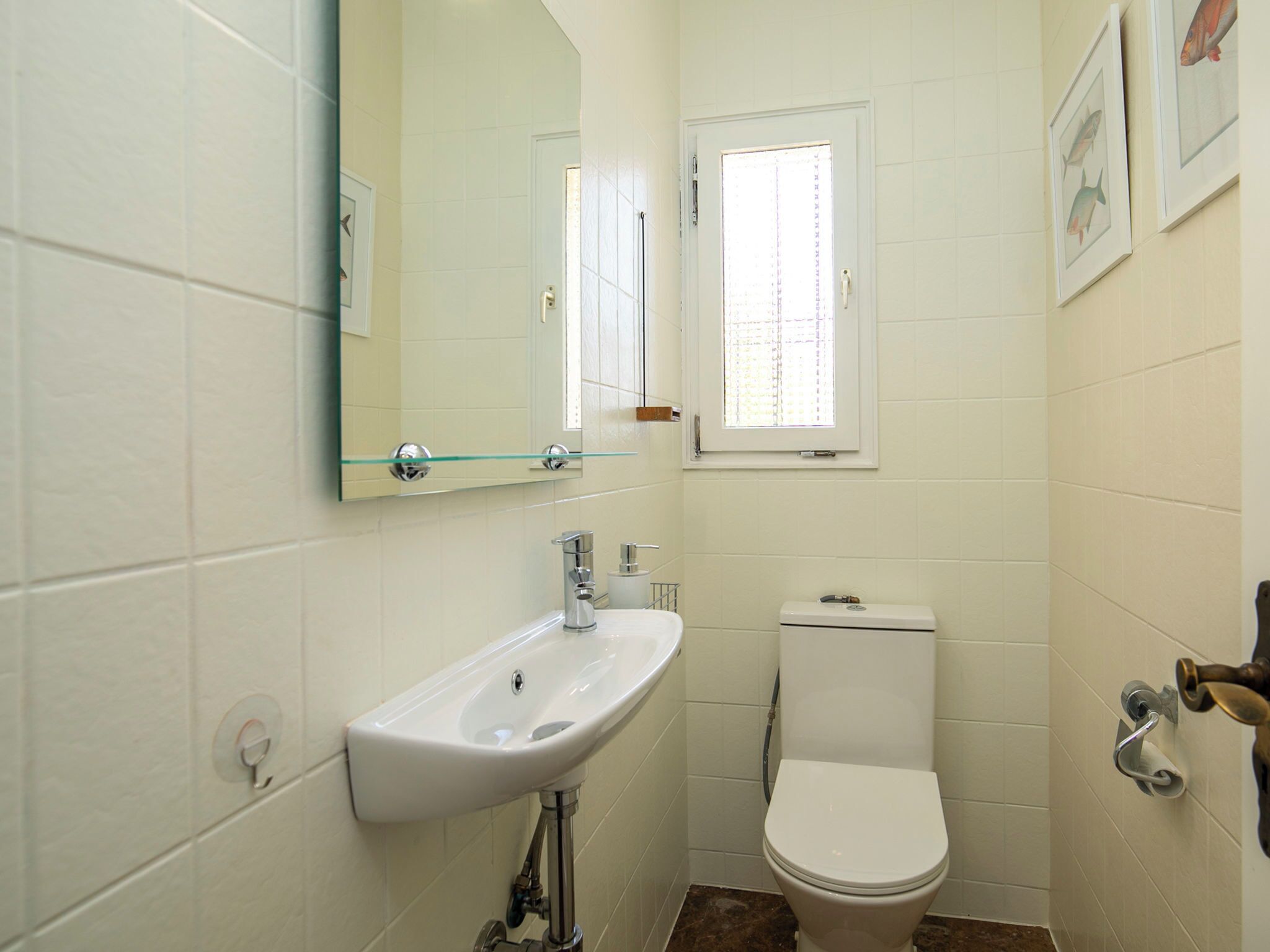 Ein Badezimmer mit einem weißen Waschbecken, einer Toilette, einem Spiegel und einem Fenster.