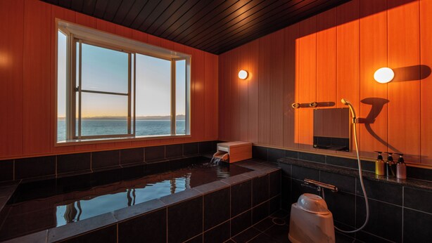 A modern bathroom with a large bathtub, a window with a view of the sea, and a shower area. - VACATION VILLA BLUE LAGOON (Numazu)