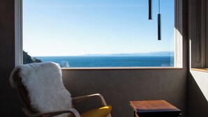 A room with a view of the ocean, a chair with a white fur throw, and a small wooden table. - VACATION VILLA BLUE LAGOON (Numazu)