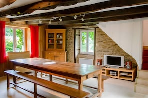 A rustic room with a wooden table, benches, a television, speakers, and a stone wall.