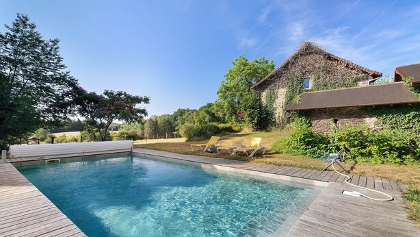 A swimming pool with a wooden deck, lounge chairs, and a stone building with ivy.