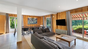A modern living room with a sectional sofa, a wooden dining table, and a TV mounted on the wall.