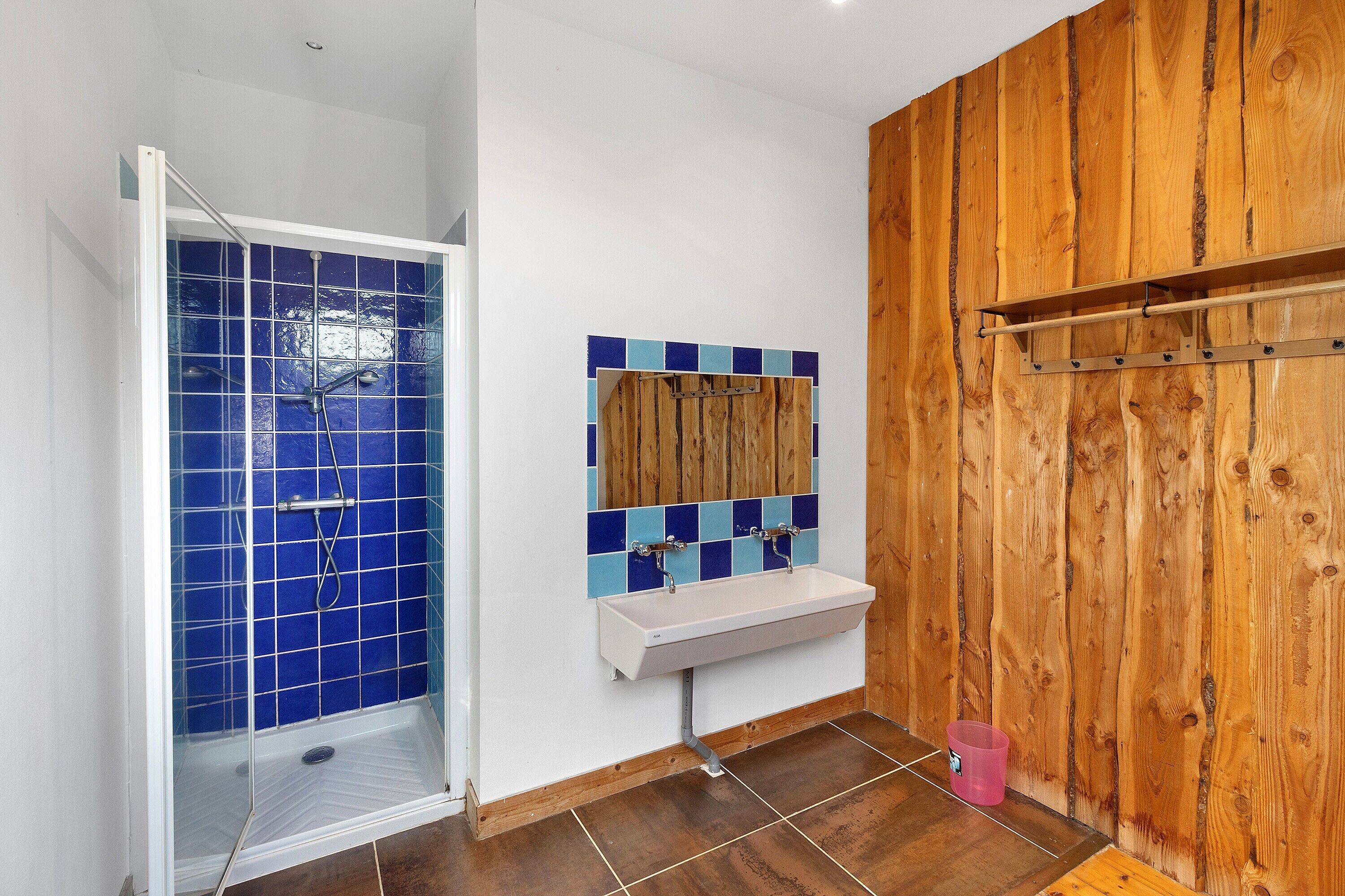 A bathroom with a shower, sink, and wooden wall paneling.