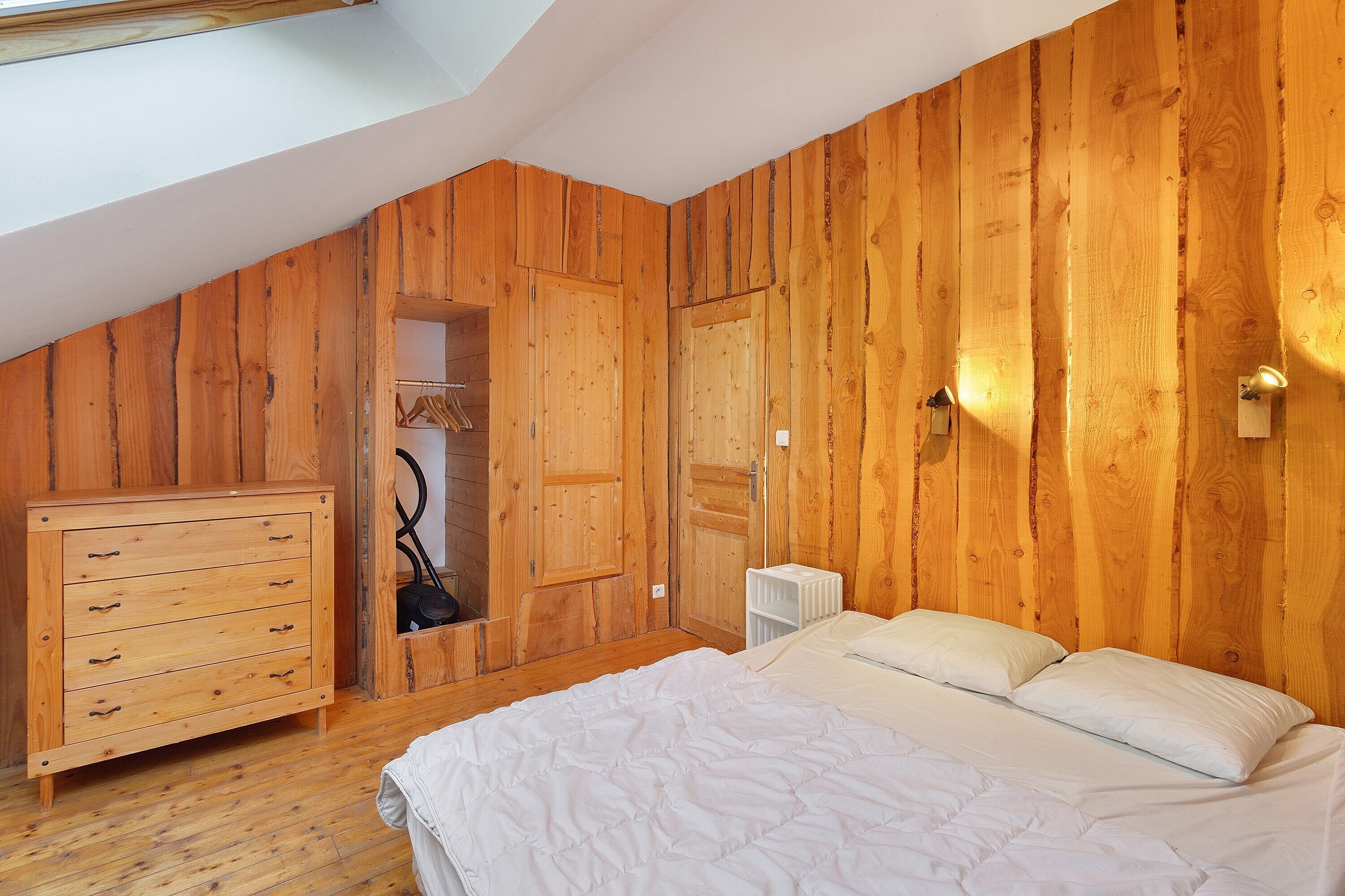 Un dormitorio con paredes de madera, una cama, un aparador y un armario.