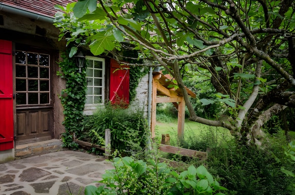 A rustic house with a stone-paved entrance, a wooden play structure, and a red door.