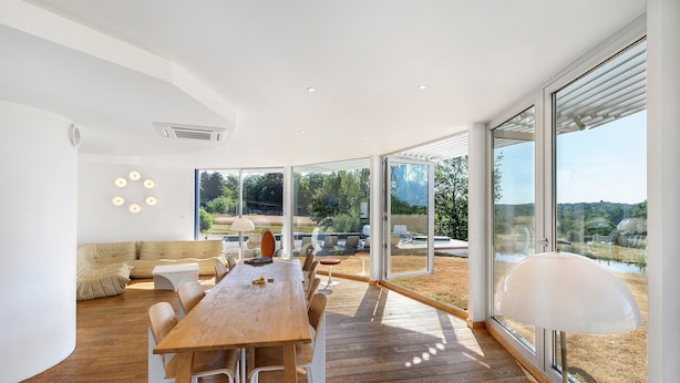 A modern interior with a wooden dining table, white chairs, a beige sofa, and large windows offering a view of the outdoors. - Modern holiday home with private pool and spa in the Périgord countryside (Angoisse)
