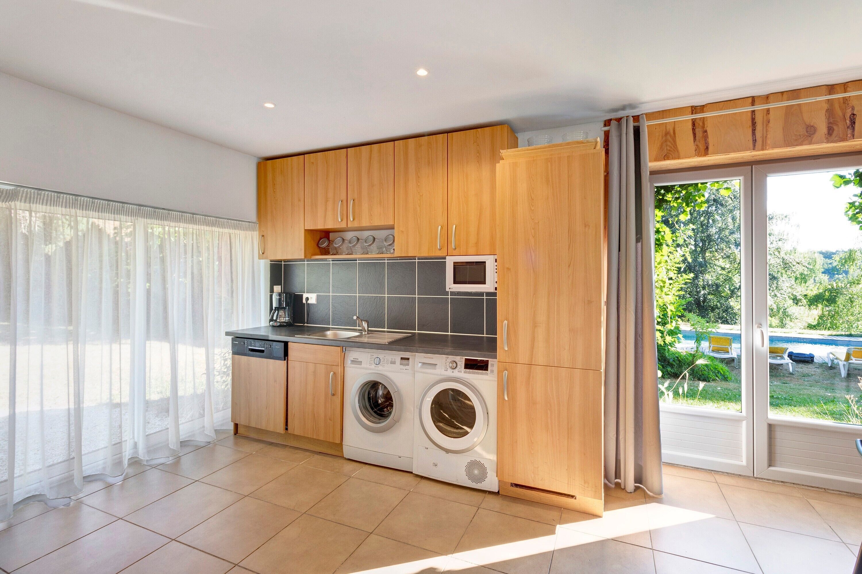A modern kitchen with built-in appliances, a washing machine, and a sliding glass door leading to a balcony.