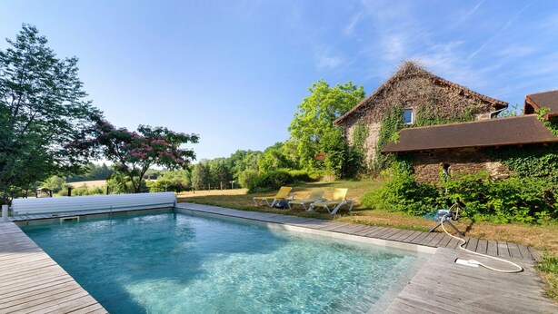 A clear swimming pool with wooden deck, lounge chairs, and a rustic stone building with ivy. - Spacious and bright holiday home in the heart of Périgord, terrace, pool & nature (Angoisse)