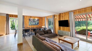 A modern living room with a sectional sofa, a dining area, and a TV mounted on the wall. - Spacious and bright holiday home in the heart of Périgord, terrace, pool & nature (Angoisse)