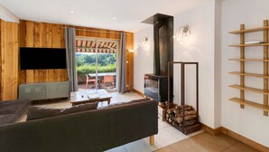A modern living room with a flat-screen TV, wooden walls, a sofa, a dining table, and a fireplace. - Spacious and bright holiday home in the heart of Périgord, terrace, pool & nature (Angoisse)