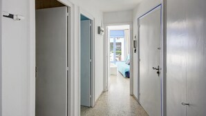 A hallway with white walls and doors, leading to a room with a bed and a view of the outside.