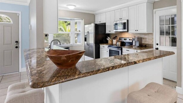 A kitchen with white cabinets, a granite countertop, a large copper bowl, and a stainless steel refrigerator.